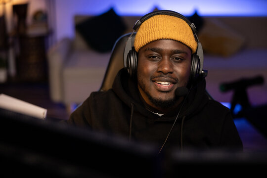 Men's Room Darkly Lit With Purple Led Lights, A Portrait From Behind A Monitor Of A Man Of American Descent Wearing A Yellow Cap With A Headset. The Guy Is Playing Shooting Games On A Computer.