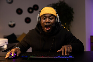 A professional computer player goes a round in a game. The man opens mouth in shock, surprise, can't believe his luck. The gamer has a headset and talks into the night with team members. © ABCreative