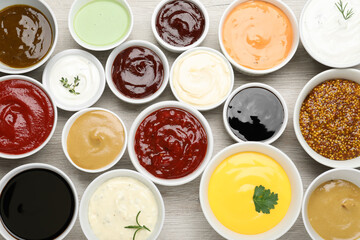 Many different sauces on white wooden table, flat lay