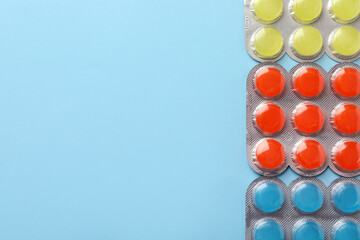 Blisters with colorful cough drops on light blue background, flat lay. Space for text