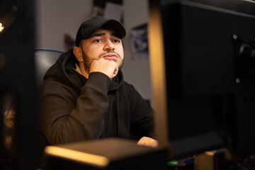 Portrait of a bearded man in black clothes hooded sweatshirt, guy works remotely at night in the IT...