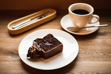 A chocolate cake with cherry filling and a cup of black coffee, selective focus natural light image
