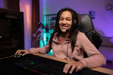 Fototapeta na wymiar Portrait of a smiling young gamer, the girl is happy to win the game, pass the level, the teenager has a headset, professional gaming accessories, the room lit by fioket blue led lights