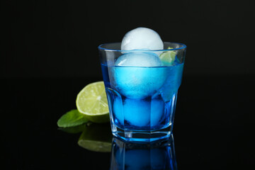 Delicious cocktail with ice balls and lime on black background