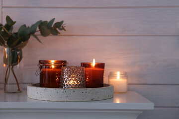 Burning candles on mantel near white wall indoors