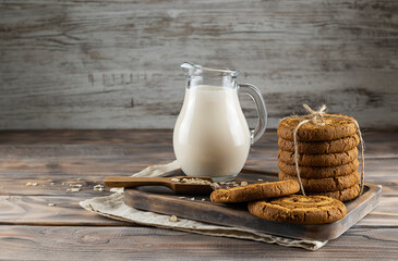 Oatmeal biscuits tied with canvas rope on a wooden tray. Oatmeal in a wooden spoon and milk in a clear jug in the background. Space for text