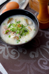 Pork boiled rice with shiitake mushrooms on a black bowl with a spoon on the table.