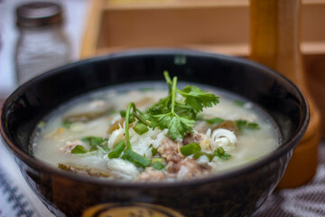 Pork boiled rice with shiitake mushrooms on a black bowl with a spoon on the table.