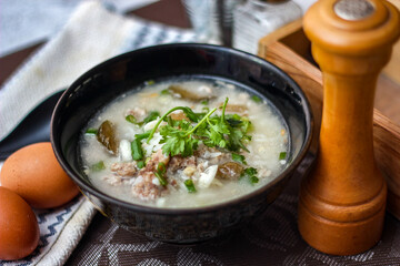 Pork boiled rice with shiitake mushrooms on a black bowl with a spoon on the table.