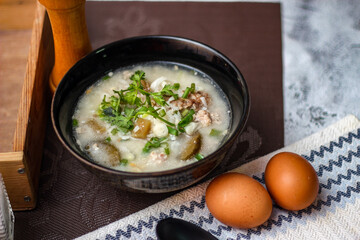 Pork boiled rice with shiitake mushrooms on a black bowl with a spoon on the table.