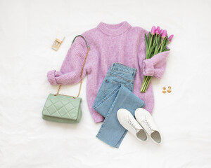Lilac knitted sweater, blue jeans, white sneakers, green bag, bouquet of tulips flower lie on white...
