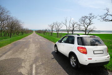 A white car after the rain stands on the side of a beautiful road that goes into the distance to...