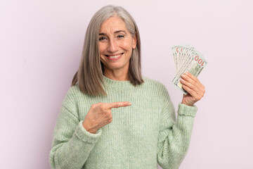 middle age woman smiling cheerfully, feeling happy and pointing to the side. dollar banknotes...