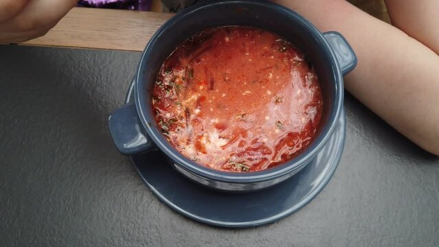 Eating borscht soup with sour cream. The point of view. Little girl is eating soup.