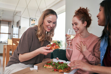 Caucasian female friends eating pizza at home and having fun