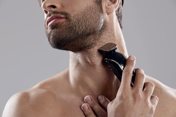Young man shaving beard with electric razor