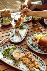 Image of table with a lot of portion of meals. Food plates with burger, shrimps, salads and drinks.