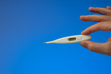 Plastic thermometer held in hand by Caucasian male. Close up studio shot, isolated on blue background
