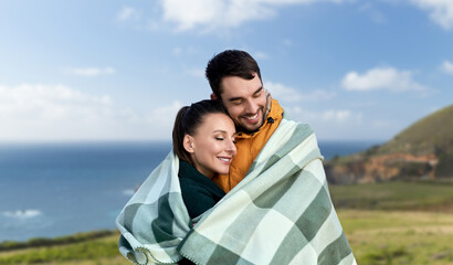 love, travel and tourism concept - happy smiling couple in warm blanket over big sur coast of california background