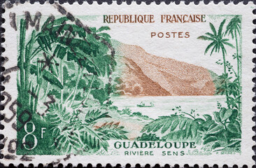 France - circa 1957: a postage stamp from France , showing a tropical landscape with palm trees and mountains at the Sens River, Guadeloupe