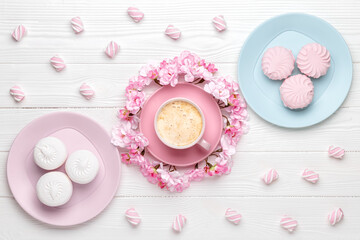 Cup of coffee and spring flowers. Dessert in the morning for breakfast, top view. Cherry blossom on a white wooden table. Flat lay design. Pastel colour card. Food and drink background. Floral decor.