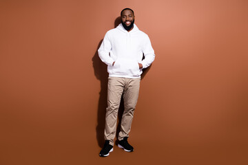 Fototapeta premium Photo of charming sweet guy wear white hoodie smiling walking hands arms pockets isolated brown color background