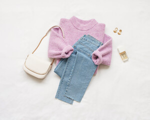 Lilac knitted sweater, blue jeans and white bag lie on white background. Overhead view of woman's...