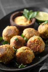 Chickpea falafel with sauce on black plate and black background close up, vertical photo