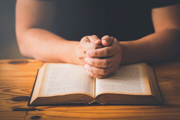 A Man Hands folded in prayer on a Holy Bible in church concept for faith, spirituality and...