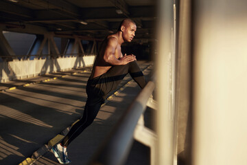 Young black sportsman stretching on empty bridge