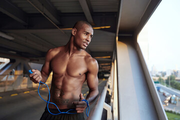 Black sportsman with skipping rope looking on city - obrazy, fototapety, plakaty