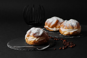 Three empty profiteroles with custard on black plates lie on a black table. Photo background - black