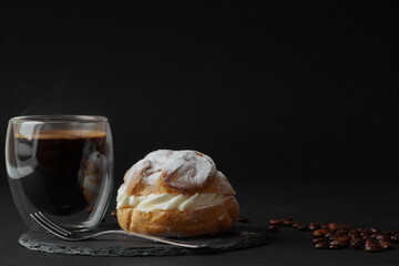a large cake - profiterole with butter cream stands on a black plate along with a cup of freshly brewed coffee. photography background - black