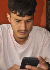 Closeup of a young guy using phone while sitting indoors