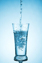 Naklejka na ściany i meble Water is poured into a transparent glass. Image on a blue background.
