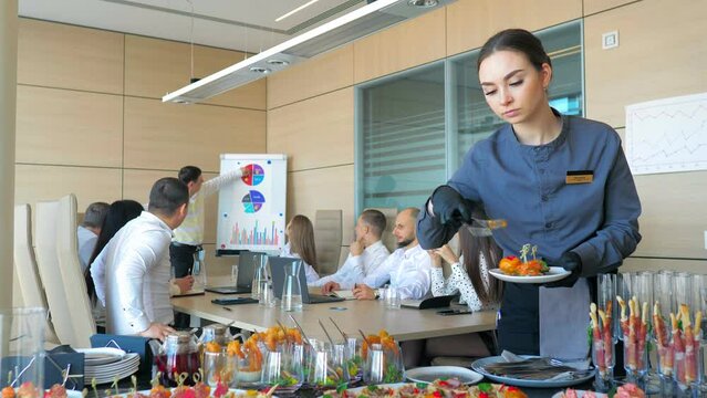 A waiter girl lays out food for catering.Beautifully decorated banquet table with canapes snacks in the office. Meals for a group of people buffet indoors.Catering business waiter.Office work,business