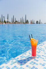 A citrus cocktail stands on the side of a blue swimming pool