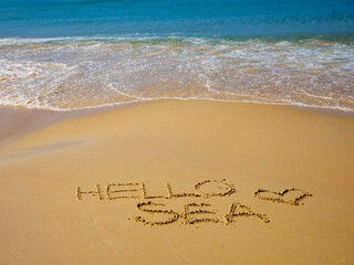 Text Hello sea handwritten on wet sand by water and rising wave on a beautiful seashore Karon beach, Phuket, Thailand. Vacation by sea, travel concept. Top aerial view