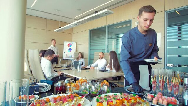 The waiter lays out food for catering.Beautifully decorated banquet table with canapes snacks in the office.Meals for a group of people on the buffet system indoors.The waiter of the catering business