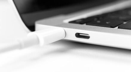 Charging battery laptop. Modern USB C port for fast charge. White cable plugged in laptop close-up...