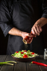 Chef adds peppers to a fresh vegetable salad in a restaurant kitchen. Close-up of cook hands holding a mill. Cooking healthy and tasty food