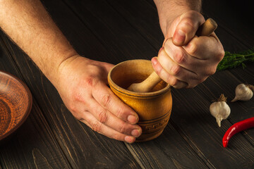 Cook crushing a blending red pepper in a wooden pestle and mortar in a close up view on his hands. Cooking a national dish in the kitchen
