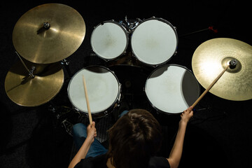 Top view of a boy learning to play the drums in the studio on a black background. A student of a...