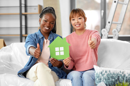 moving, people and real estate concept - happy smiling women holding green house and showing thumbs up at new home