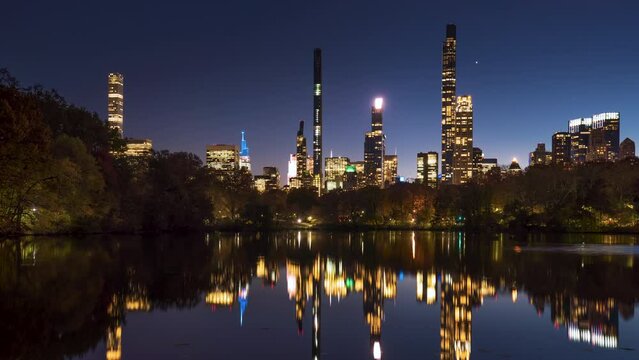 Central Park Lake with view of New York City Billionaire's Row from dusk to night. Timelapse citiscape of luxury apartment skyscrapers
