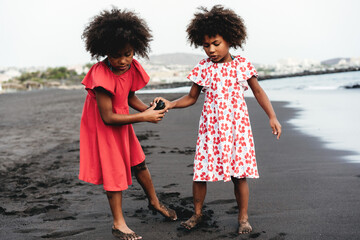Afro twin sisters having fun on the beach playing with a rock - Focus on right girl face