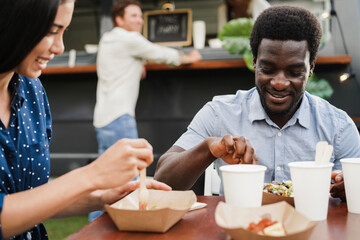 Fototapeta na wymiar Multiracial couple having fun eating at food truck restaurant outdoor - Focus on african man face