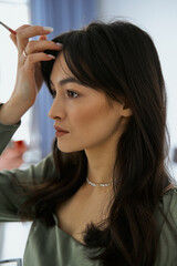 Fototapeta premium Lovely beautiful girl with an eyebrow brush in her hand looks in the mirror.