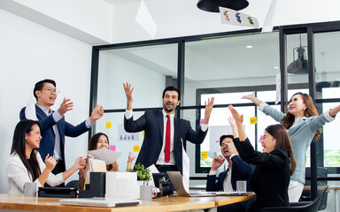 Mixed race business people wearing formal suits, throwing papers to celebrate their success and happiness in jobs and done their projects while sitting in meeting room in indoor office or workplace.