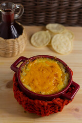 Cheese sauce in a red saucepan, next to chips and a bottle of red juice. Rustic style